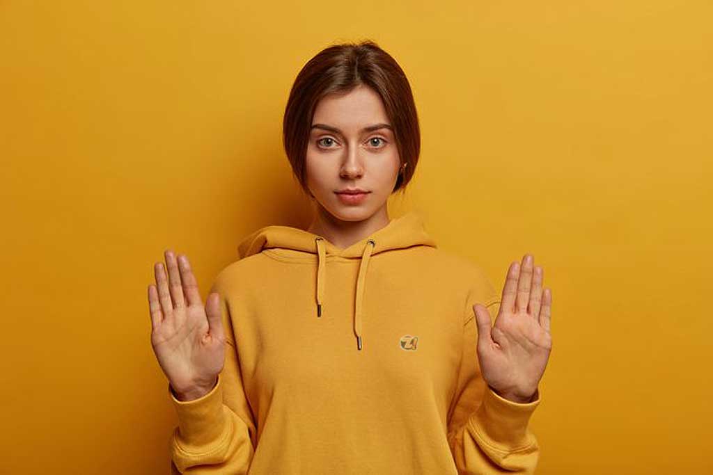 Mulher jovem, morena, vestindo blusa amarela, com expressão séria e demonstrando discordância.