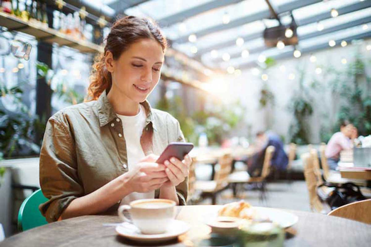 Mulher jovem atualizando suas redes sociais usando um celular.