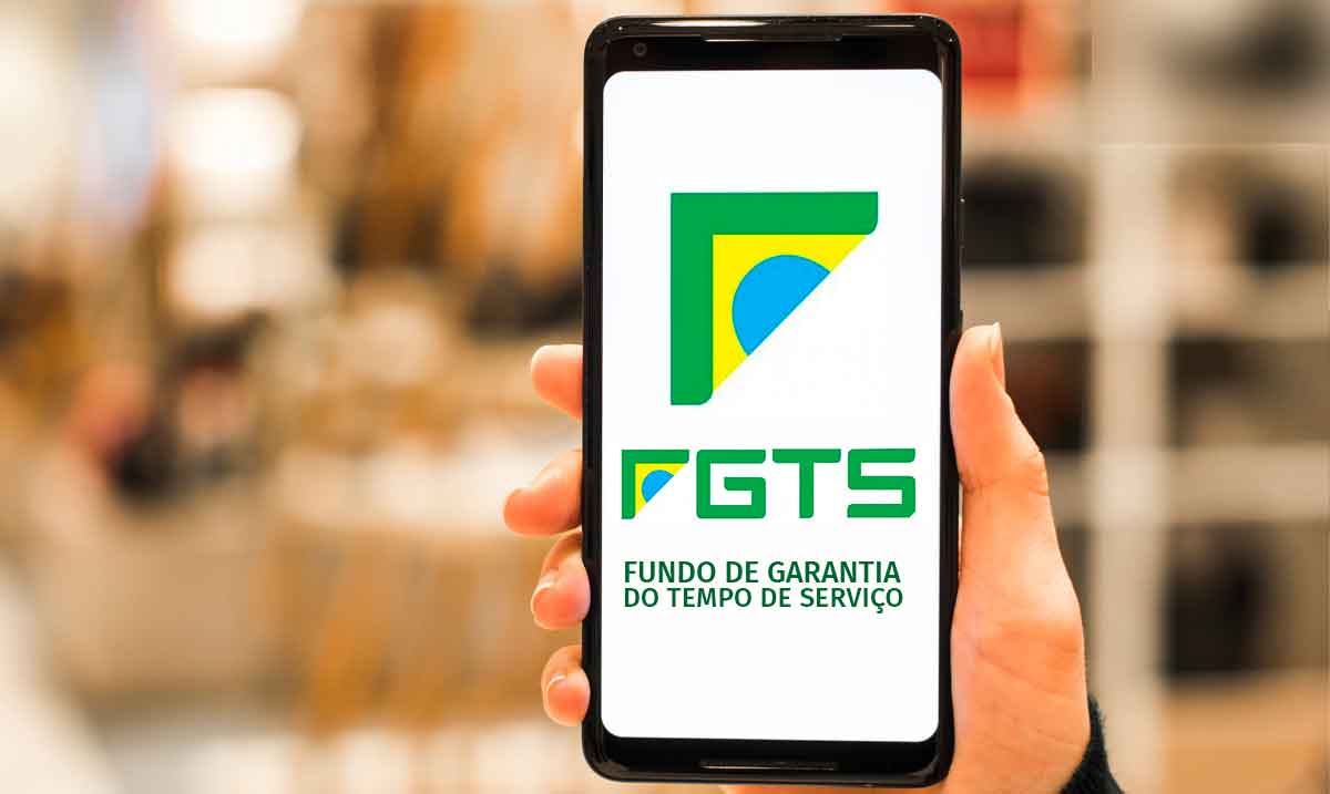 Uma pessoa usando app do FGTS na frente de um notbook com site da Caixa aberto.